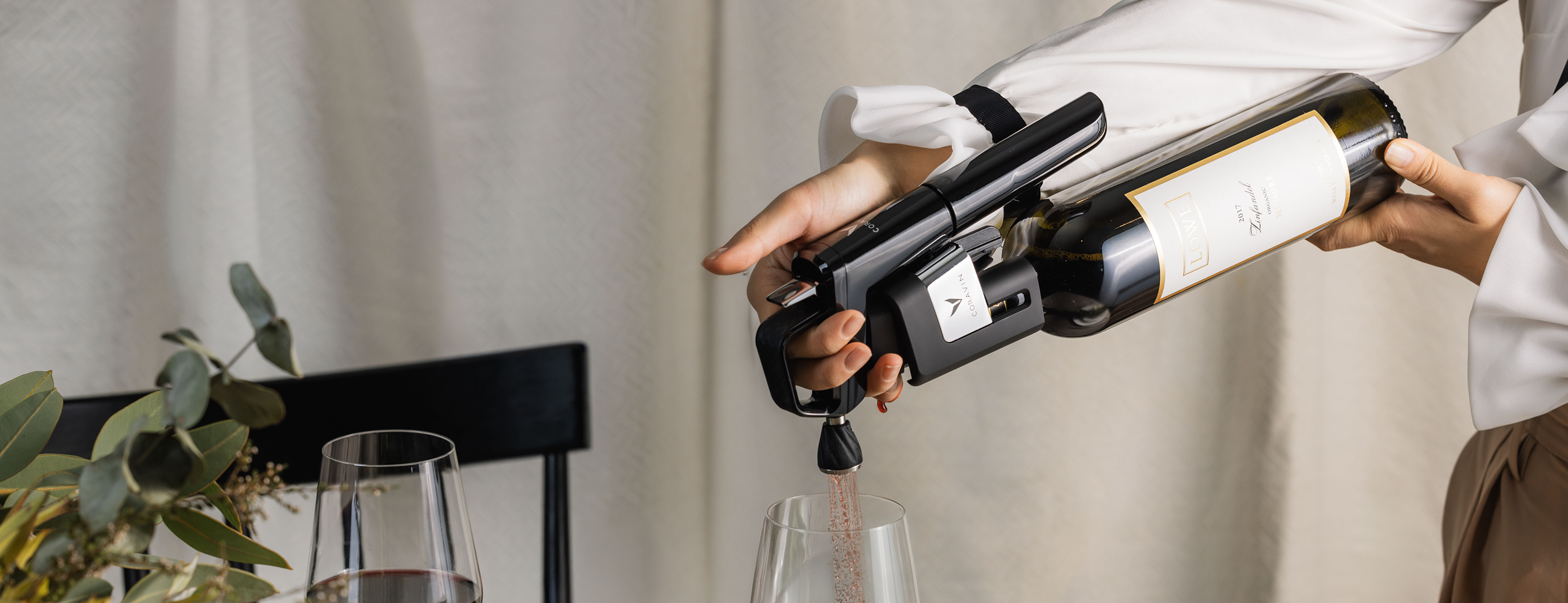 A hand using a Coravin wine preservation system to pour wine into a glass, with a bottle labeled "Lowe 2017 Zinfandel."