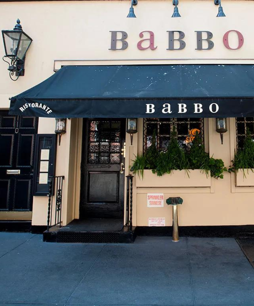 Exterior of Babbo Ristorante with a dark awning, vintage lanterns, and green plants in window boxes along a cream-colored facade.