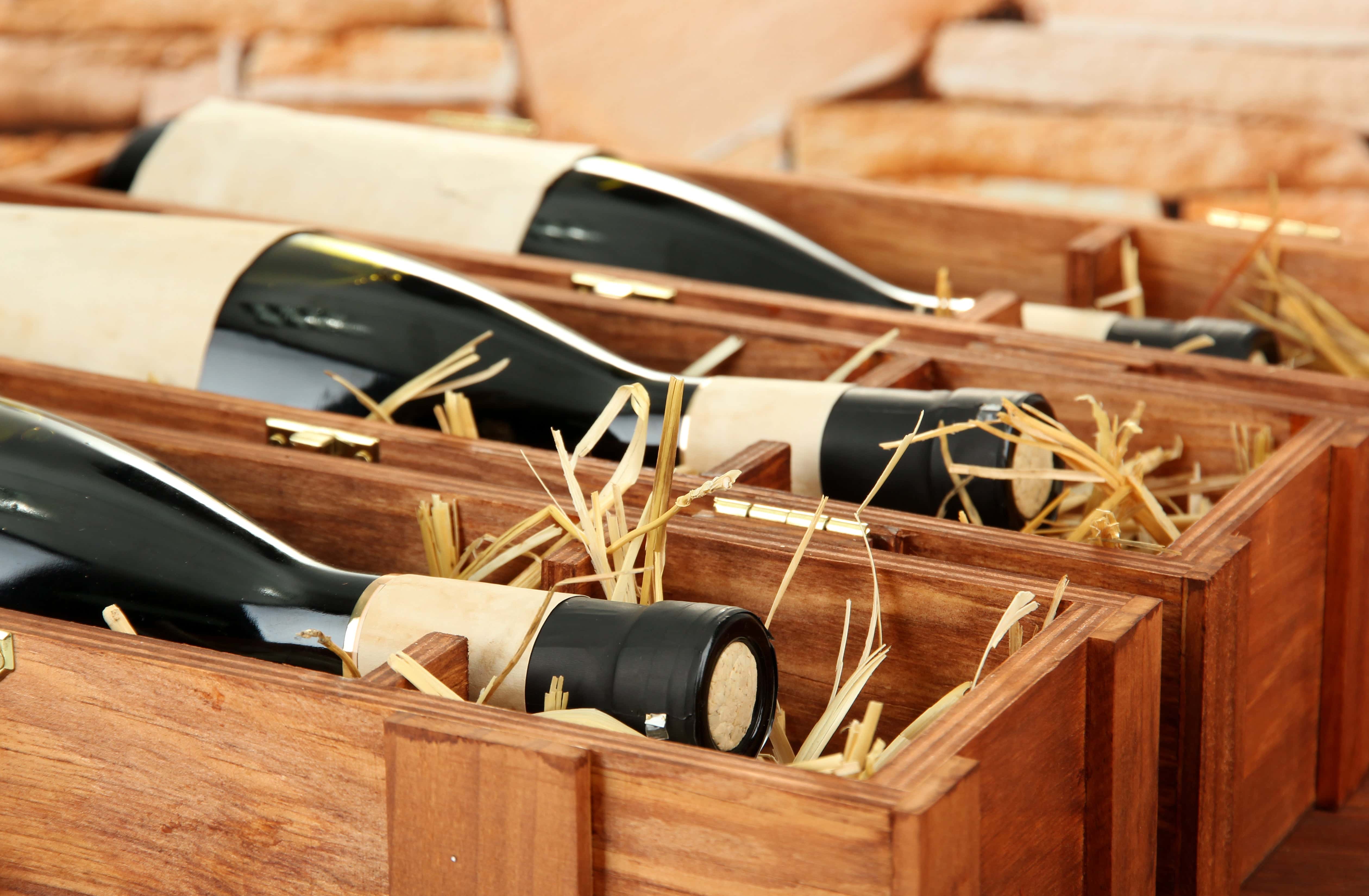 Close-up of several wine bottles lying in individual wooden gift boxes filled with straw for cushioning, creating an elegant presentation for gifting or storage.