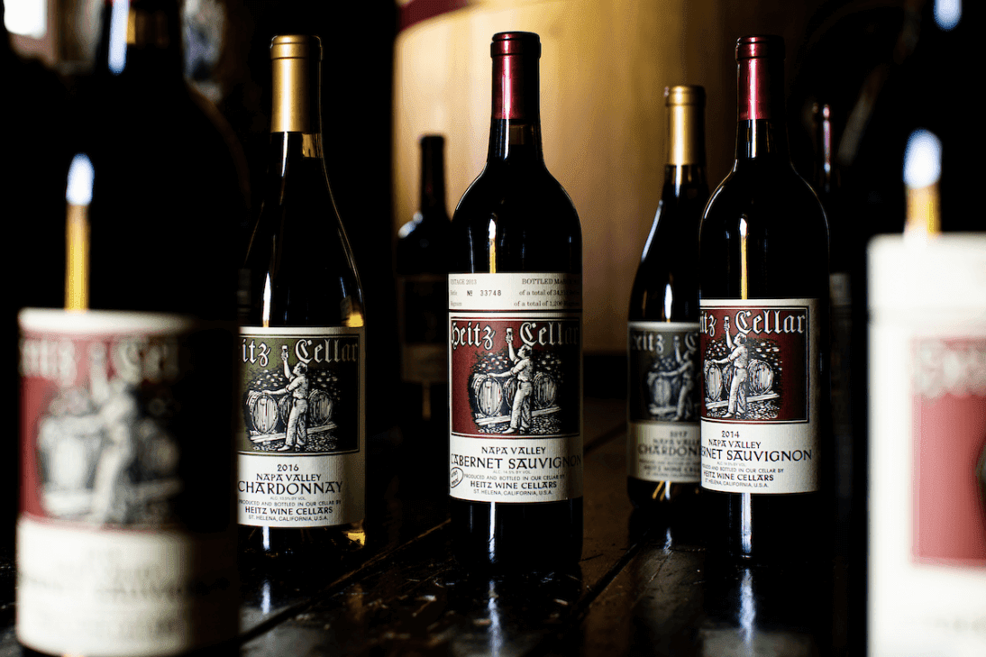 Bottles of Heitz Cellar Napa Valley wines, including Cabernet Sauvignon and Chardonnay, displayed on a wooden surface in dim cellar lighting.