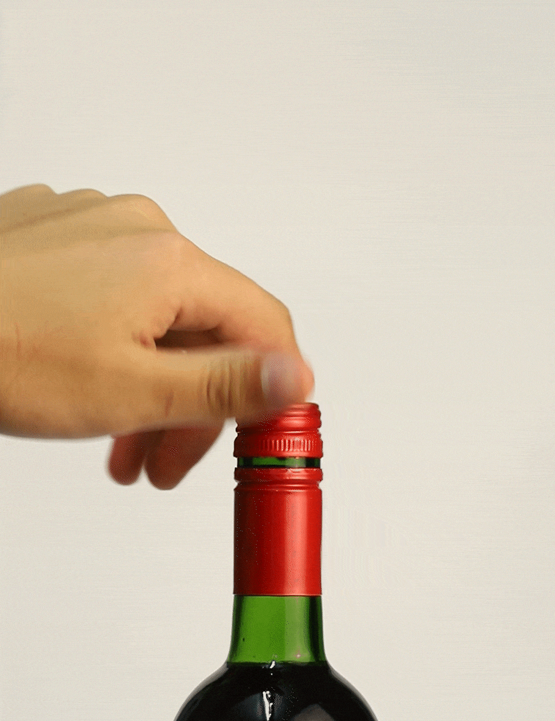A hand twists off the red cap of a wine bottle, revealing the green neck and label reading "Woodbridge."